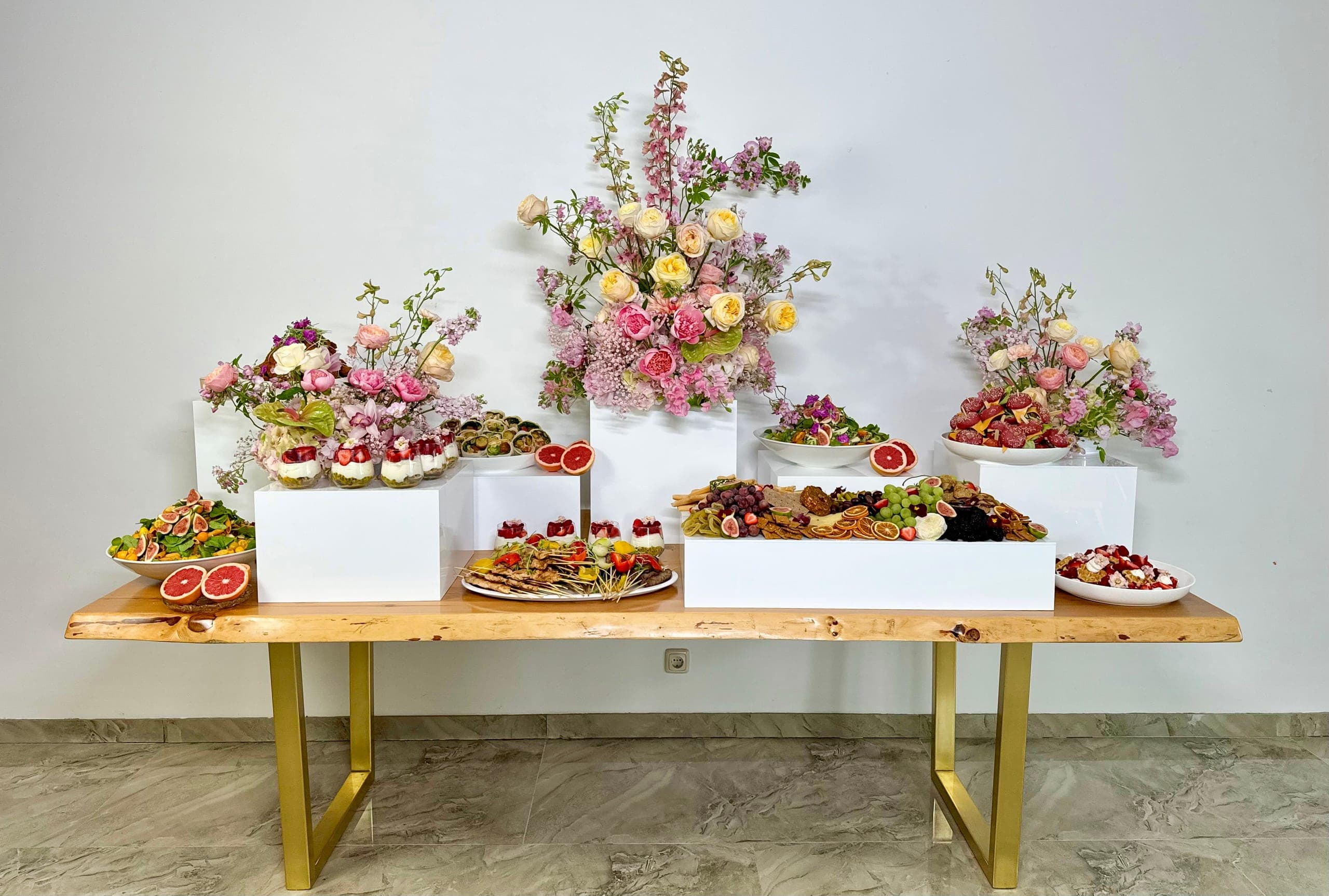 Grazing-Tisch aus Holz mit Messinggestell: Käse- und Cracker-Platte, Häppchen und pastellfarbene Blumengestecke