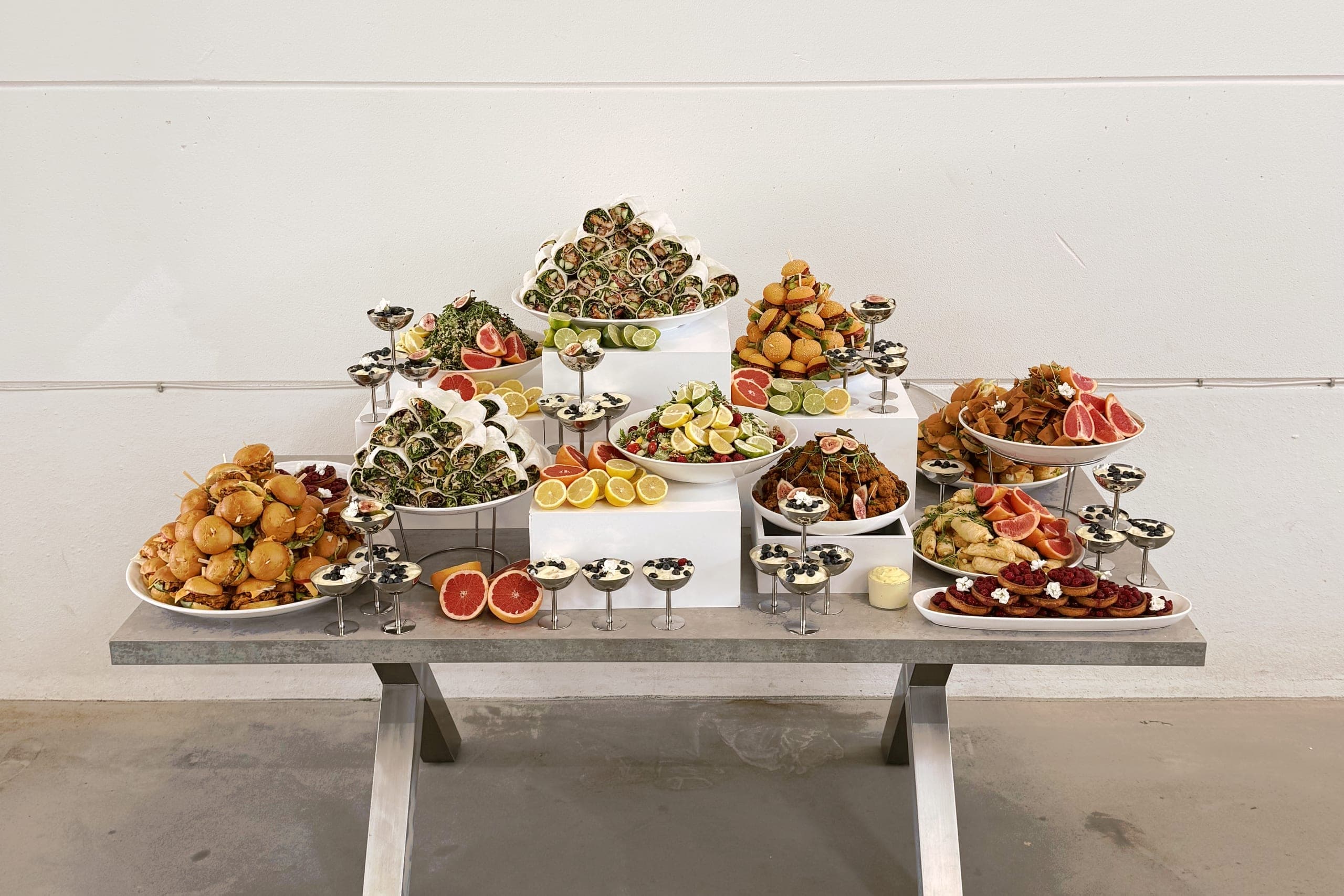 Buffettisch frontal vor heller Wand: Wrap-Pyramide in der Mitte, Mini-Burger links, warme Häppchen und Salate rechts, Dessertgläser vorn