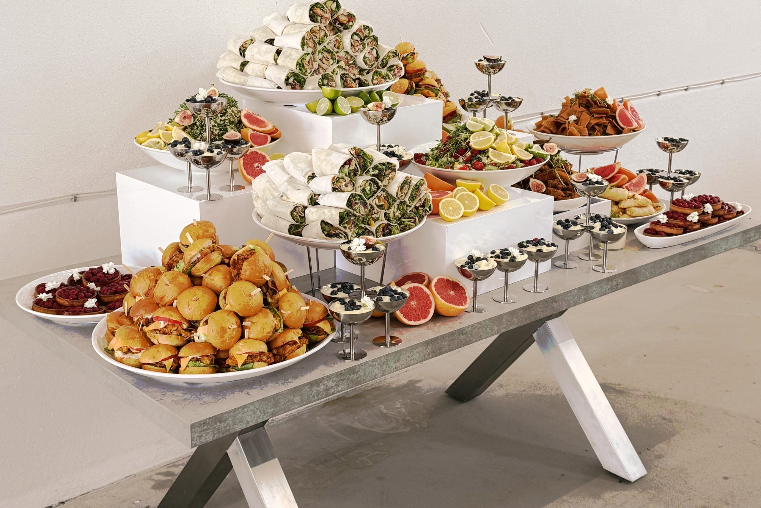 Ganzer Buffettisch für ein Firmenevent: Wraps auf zwei Etagen, Mini-Burger, Salate mit Grapefruit und Zitrone, Dessertgläser auf Ständern, Tartelettes mit Himbeeren